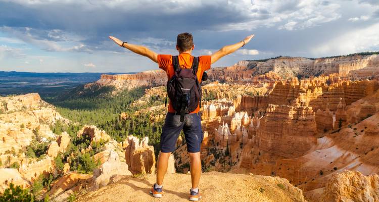 Persoon staand met uitgestrekte armen uitkijkend over Bryce Canyon.