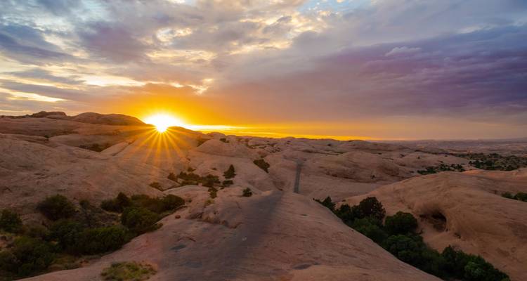 Zonsondergang boven een woestijnlandschap met rotsachtige heuvels.