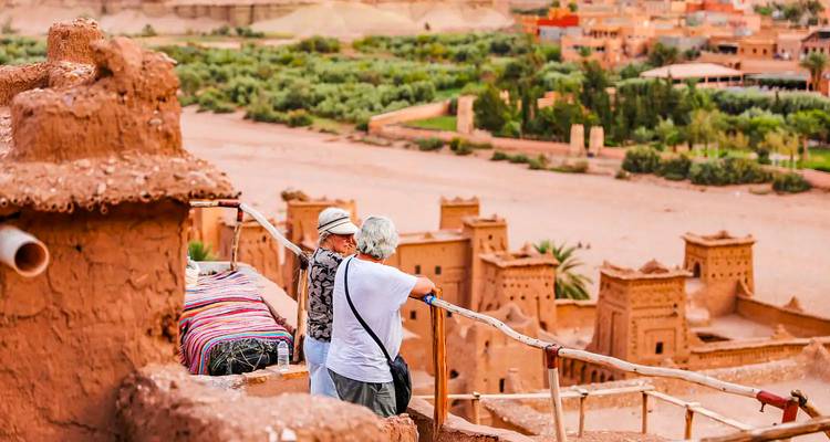 Two travellers admire the clay kasbahs of Ait Benhaddou from a scenic overlook above the river.