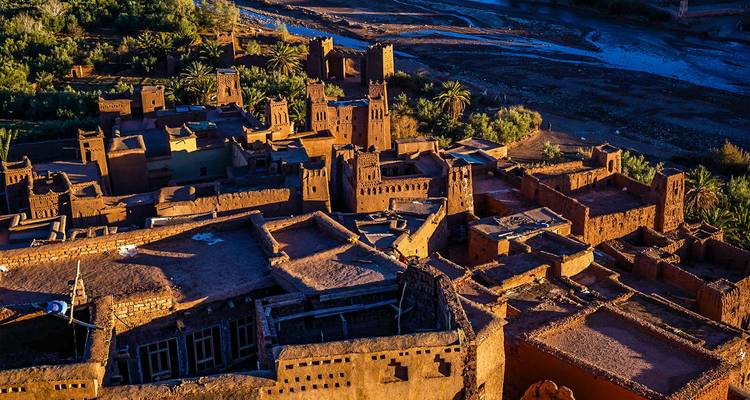 Golden-hour aerial view over the fortified ksar of Ait Benhaddou and its surrounding riverbed.
