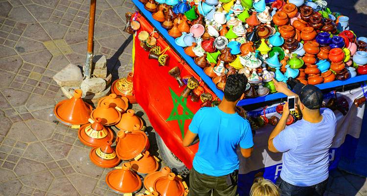 Overhead market stall piled with colorful miniature tagine pots and Moroccan flag bunting.