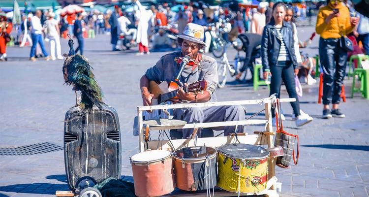 Street musician plays guitar and drums in a vibrant public square full of onlookers.