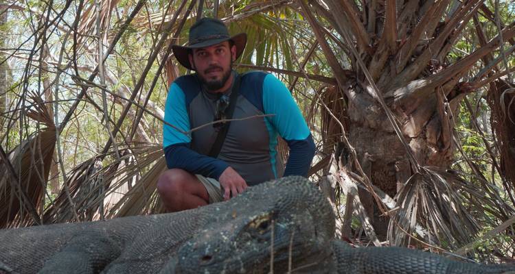 Mann posiert mit einem Komodowaran in einer Waldumgebung.