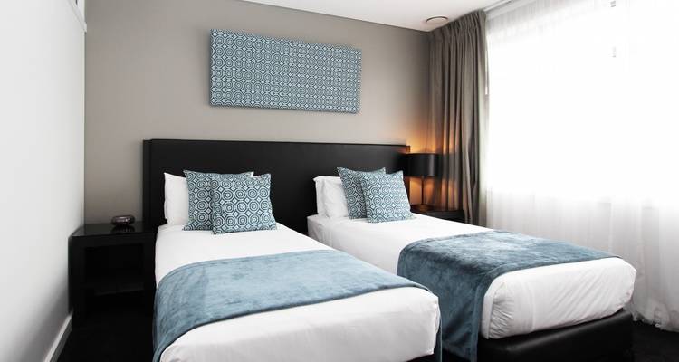 A hotel room with two single beds and modern decor.