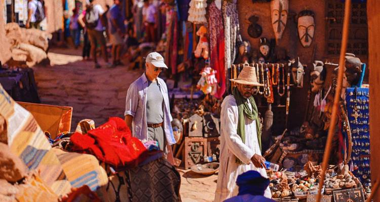 Mercado al aire libre en un pueblo con paredes de adobe con puestos de artesanías, máscaras y textiles.