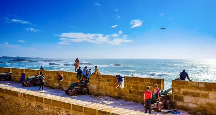 Los visitantes se paran en las murallas junto al mar mirando cómo las olas se estrellan contra el Atlántico en Essaouira.