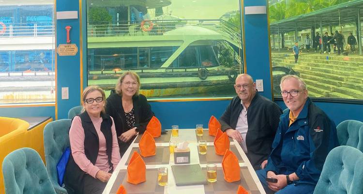 Petit groupe de touristes assis autour d'une table avec des boissons à l'intérieur d'un bateau de croisière moderne de la baie d'Halong