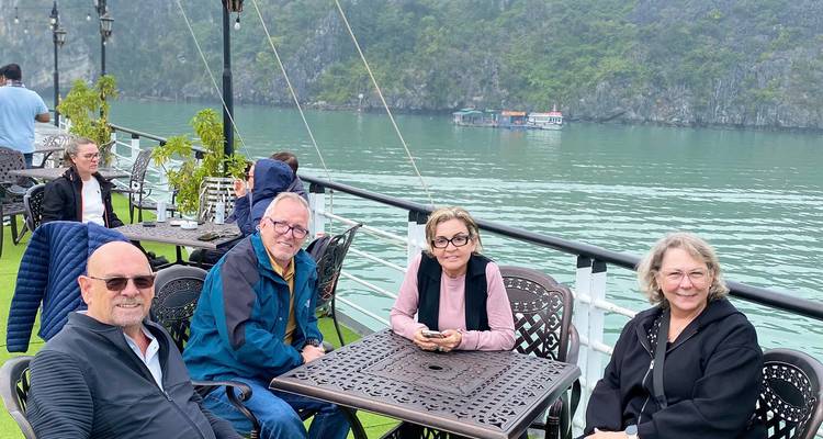 Les voyageurs sont assis sur le pont ouvert d'un bateau naviguant dans les eaux vertes karstiques de la baie d'Halong