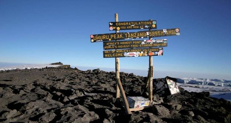 Ein Schild, das den Uhuru Peak am Mount Kilimanjaro unter klarem Himmel markiert.