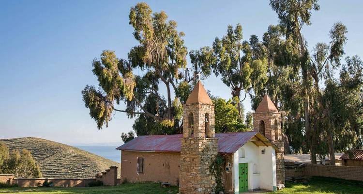 Petite église en pierre entourée d'arbres avec des collines en arrière-plan.