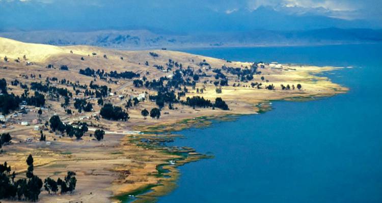 Côte avec eau et collines lointaines, ciel dégagé.