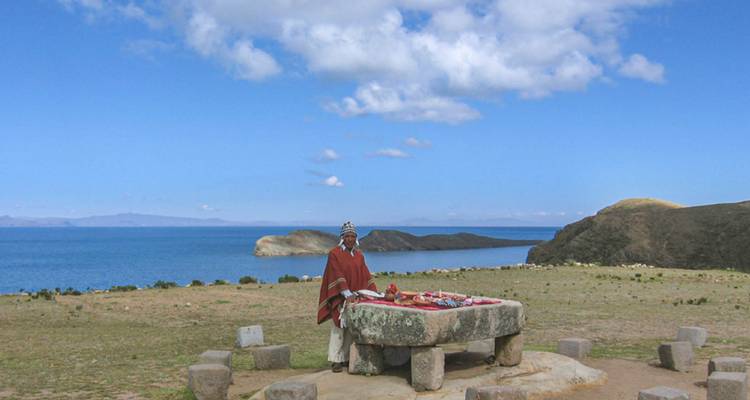 Personne en vêtements traditionnels debout près d'une structure en pierre avec un lac en arrière-plan.