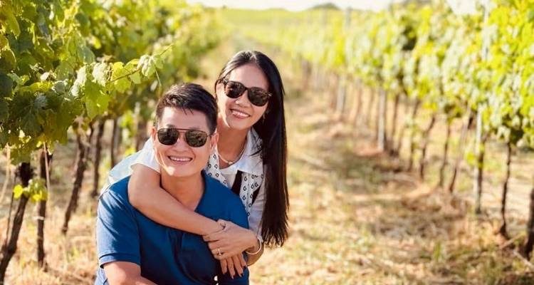 Couple souriant portant des lunettes de soleil posant dans un vignoble ensoleillé.