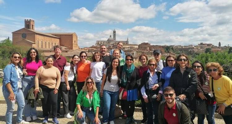 Grand groupe de touristes posant avec la ville de Sienne visible sur la colline derrière eux.
