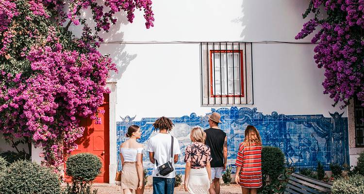 Grupo de viajeros admira un mural de azulejos azul vívido enmarcado por buganvillas en flor en Lisboa.