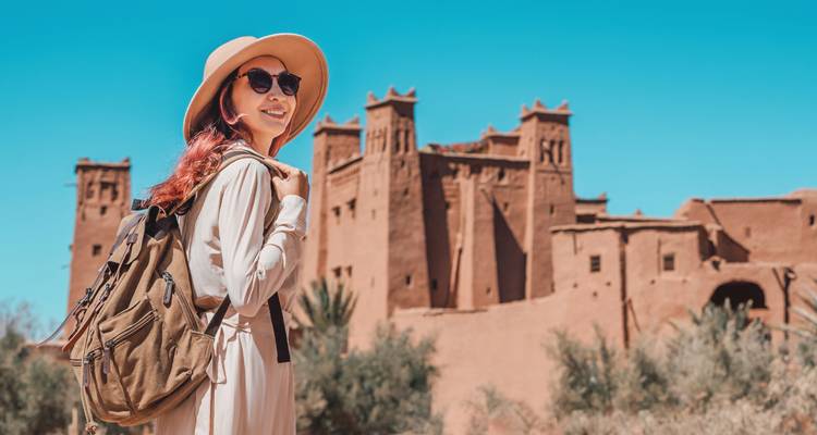 Voyageuse avec sac à dos souriante devant la Kasbah en terre crue d'Ait Benhaddou