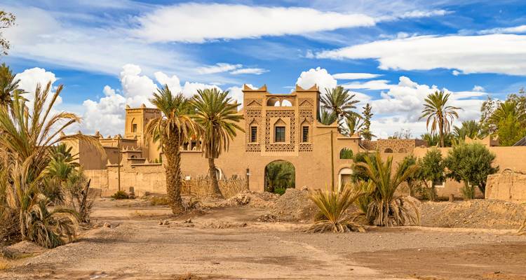 Complexe traditionnel de kasbah marocaine avec palmiers et ciel partiellement nuageux
