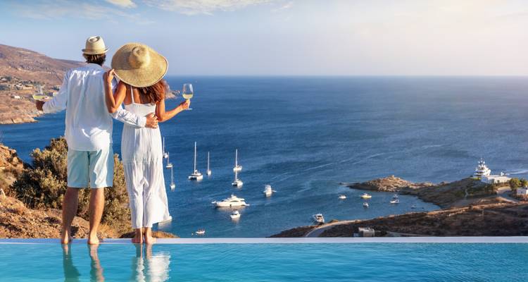 Un couple romantique trinquant avec du vin à une piscine à débordement surplombant une baie parsemée de yachts.