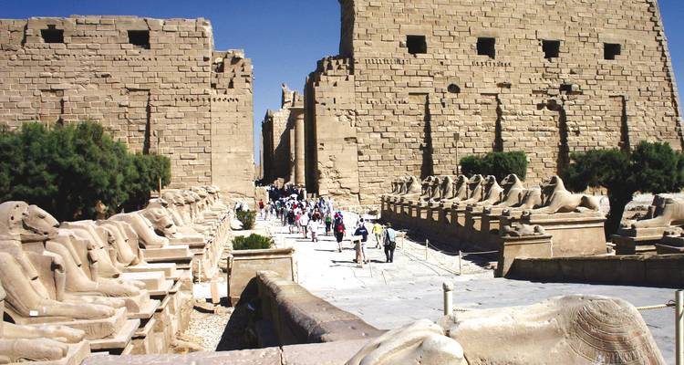 Des touristes marchant entre des ruines antiques bordées de sphinx.
