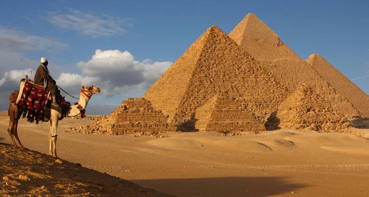 Un jinete de camello observa las Pirámides de Giza bajo un cielo de tarde brillante.