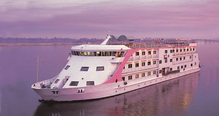 Un gran barco de crucero por el Nilo blanco y rosa se desliza sobre las tranquilas aguas del río bajo un cielo de atardecer en tonos pastel.