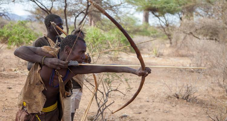 Indigenous people using bows and arrows in a natural setting.