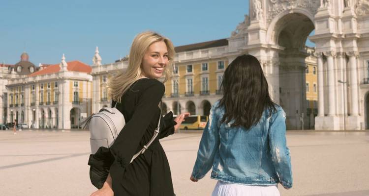 Deux voyageuses traversent la Praça do Comércio de Lisbonne avec l'imposant Arc de la Rua Augusta en arrière-plan.