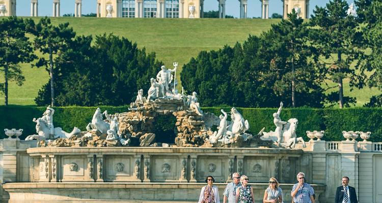 Reisegruppe geht an dem kunstvollen Neptunbrunnen vorbei mit dem Gloriette-Hügel von Schloss Schönbrunn im Hintergrund.