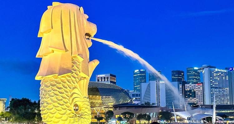 Merlion-standbeeld verlicht in de nacht met een stadshorizon.