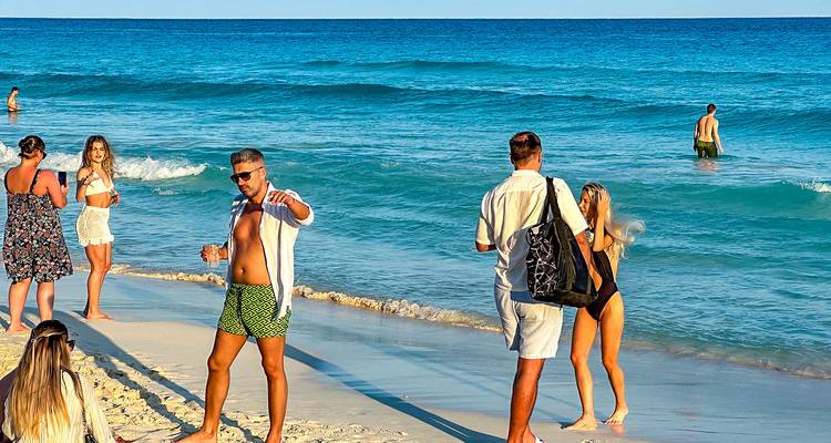 Mensen die genieten van een dagje strand met golven en een heldere hemel.
