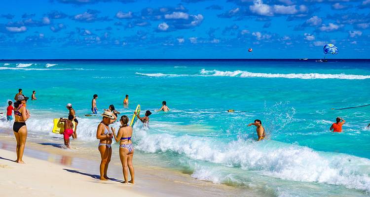 Druk strand met helder turquoise water en parasailen.