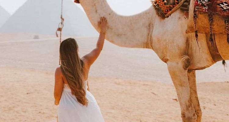 Femme avec un chameau dans le désert, pyramides au loin.