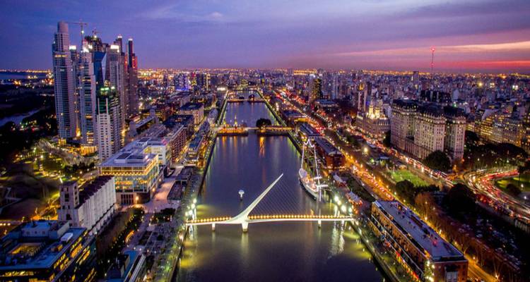 Paisaje urbano nocturno con un puente iluminado sobre un río.