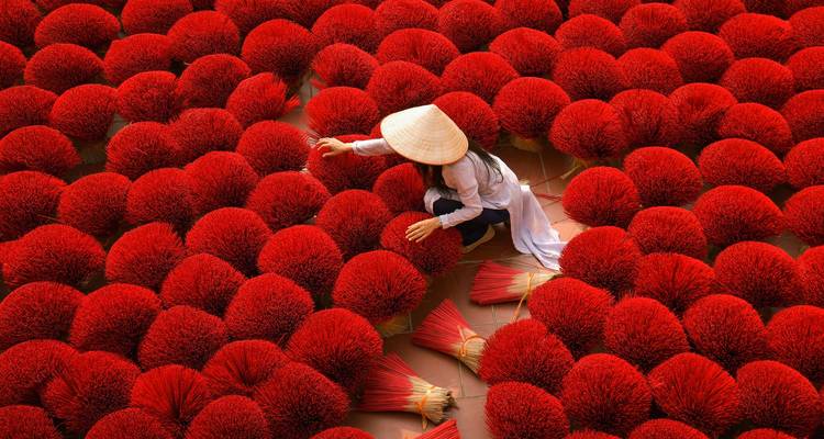 Femme arrangeant des bâtons d'encens rouges dans un cadre extérieur vibrant.