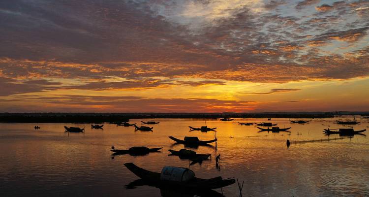 Coucher de soleil sur une rivière calme avec des bateaux en silhouette.