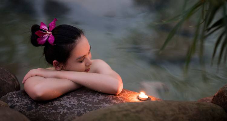 Femme se relaxant dans l'eau avec une fleur et une bougie à proximité.