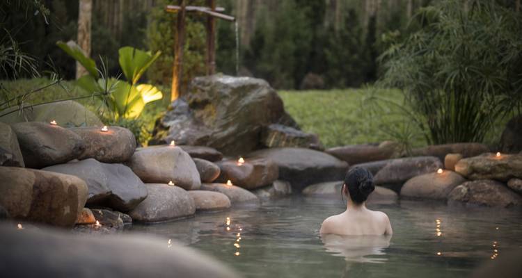 Personne profitant d'une source chaude naturelle avec des bougies autour.