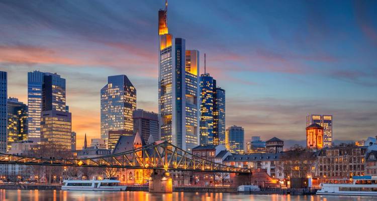 Horizonte de la ciudad con un río y edificios iluminados al anochecer.