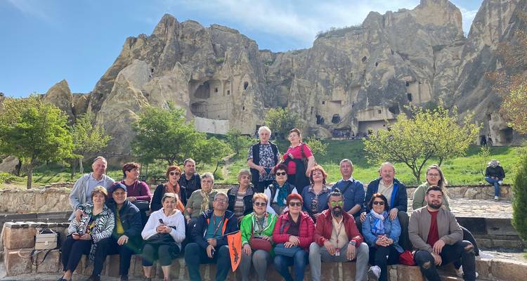 Grote groep poseert met rotsgrotten op de achtergrond.
