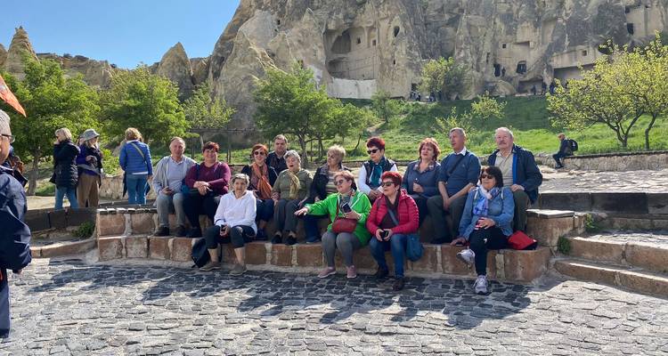 Kleine groep zittend op stenen treden voor rotsformaties.