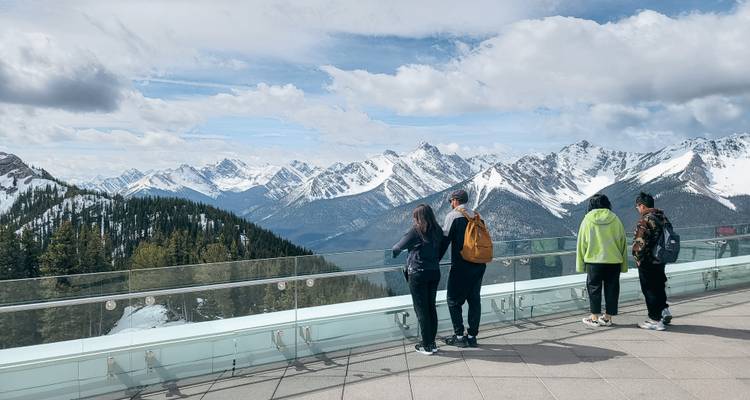 Mensen die op een uitkijkplatform staan met uitzicht op een besneeuwde bergketen.