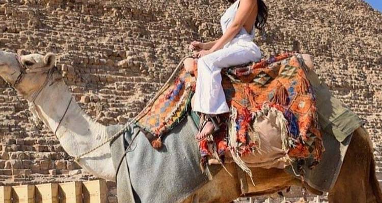Person riding a camel near the pyramids on a sunny day.