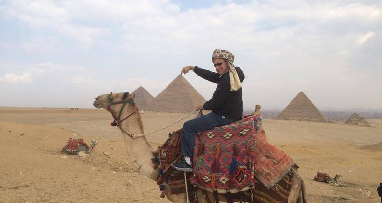 Person riding a camel in front of the pyramids.