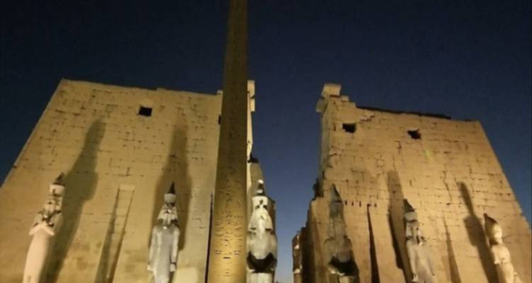 Beleuchtete Ruinen bei Nacht mit Statuen am Eingang.