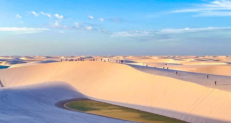 Weids uitzicht over bleke zandduinen bezaaid met kleine wandelaars en een turquoise lagune in Lençóis Maranhenses