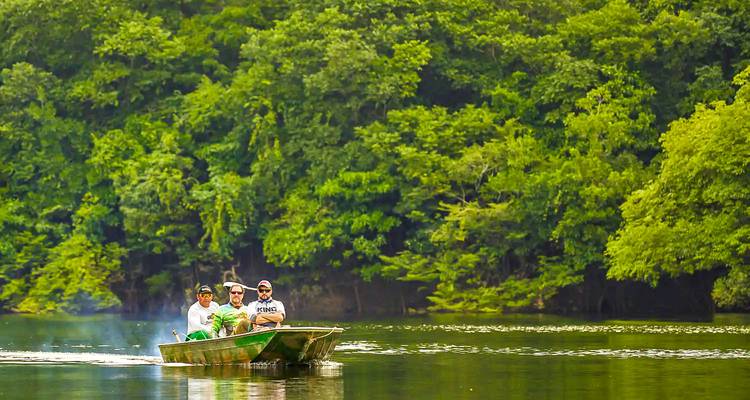 Kleine motorboot met toeristen glijdt langs een rustige Amazone rivier omringd door weelderige jungle