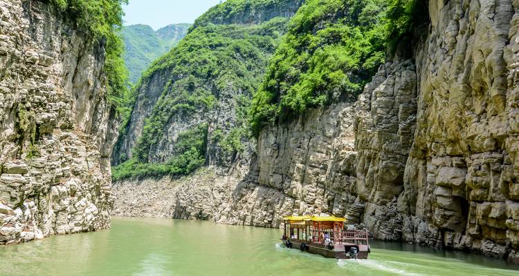 Ein Ausflugsboot fährt durch eine steile grüne Schlucht mit hohen Kalksteinfelsen, die auf beiden Seiten aufragen.