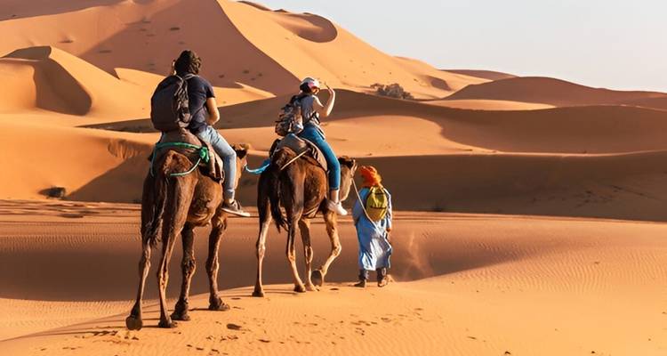 Deux personnes sur des chameaux dans le désert avec des dunes de sable.