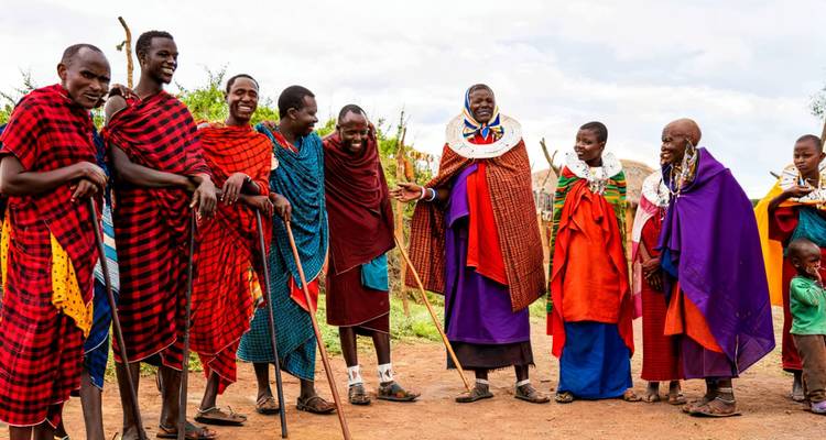 Membres de la communauté Maasaï discutant et riant ensemble en tenue traditionnelle rouge et violette dans un cadre villageois.
