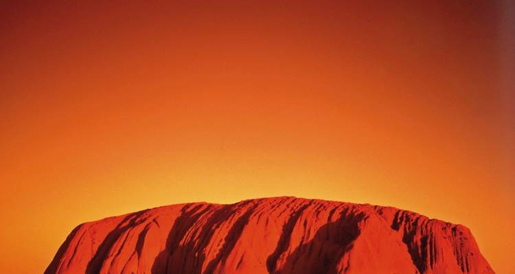 Ulurus massiver roter Sandstein-Monolith glüht unter einem leuchtend orangefarbenen Himmel.